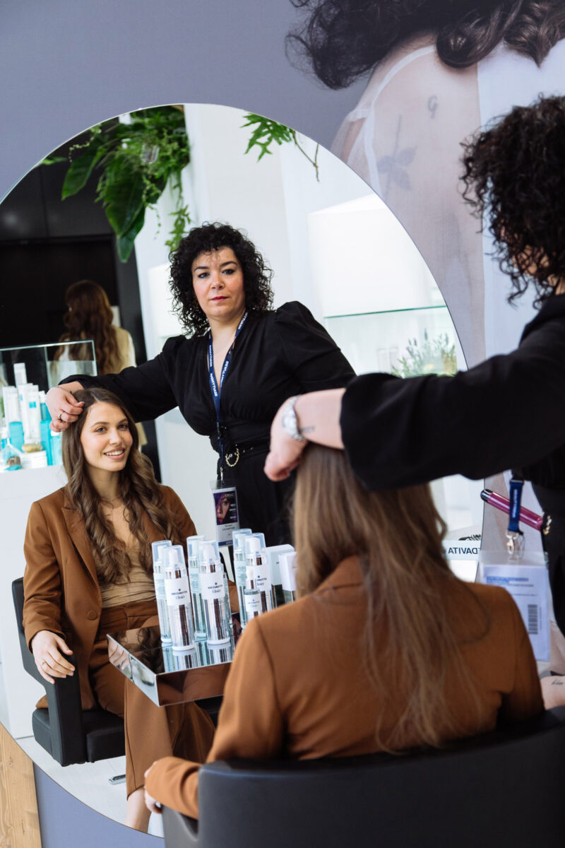 Dimostrazione haircare a Cosmoprof Bologna: consulenza in salone con prodotti professionali e styling davanti allo specchio