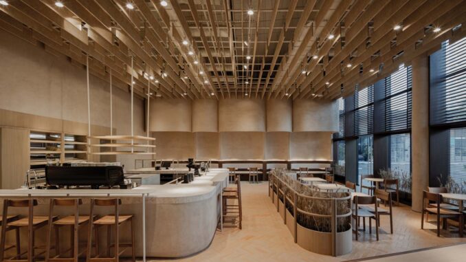 Interni della panetteria di design Krume Bäcker a Panama, con bancone in terra compattata, arredi in legno recuperato e soffitto a listelli. Interior view of Krume Bäcker design bakery in Panama, featuring a rammed earth counter, reclaimed wood furniture, and slatted ceiling structure.