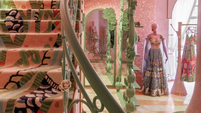 Interno del flagship store Papa Don’t Preach a Delhi con scala scultorea, pavimenti decorativi, manichini couture e palette cromatica rosa e verde Interior of the Papa Don’t Preach flagship store in Delhi featuring a sculptural staircase, decorative flooring, couture mannequins and a pink-and-green color palette