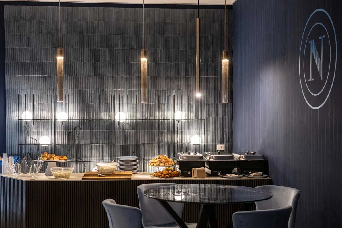 bancone buffet con illuminazione verticale dorata e rivestimenti blu nella Hospitality Lounge