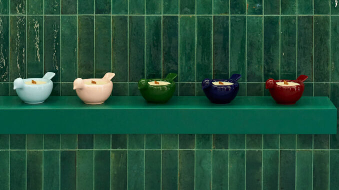 Detail of handcrafted GUNIA Project ceramics displayed on a green shelf against a tiled ceramic wall