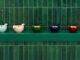 Detail of handcrafted GUNIA Project ceramics displayed on a green shelf against a tiled ceramic wall