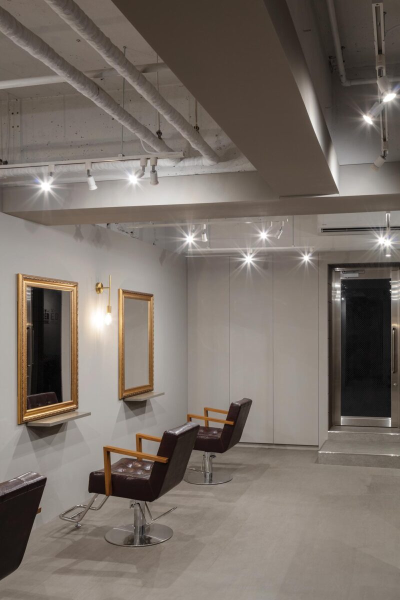 Cutting stations at RED Hair Design in Tokyo with dark leather chairs, gold-framed mirrors and track lighting in a minimalist hair salon interior