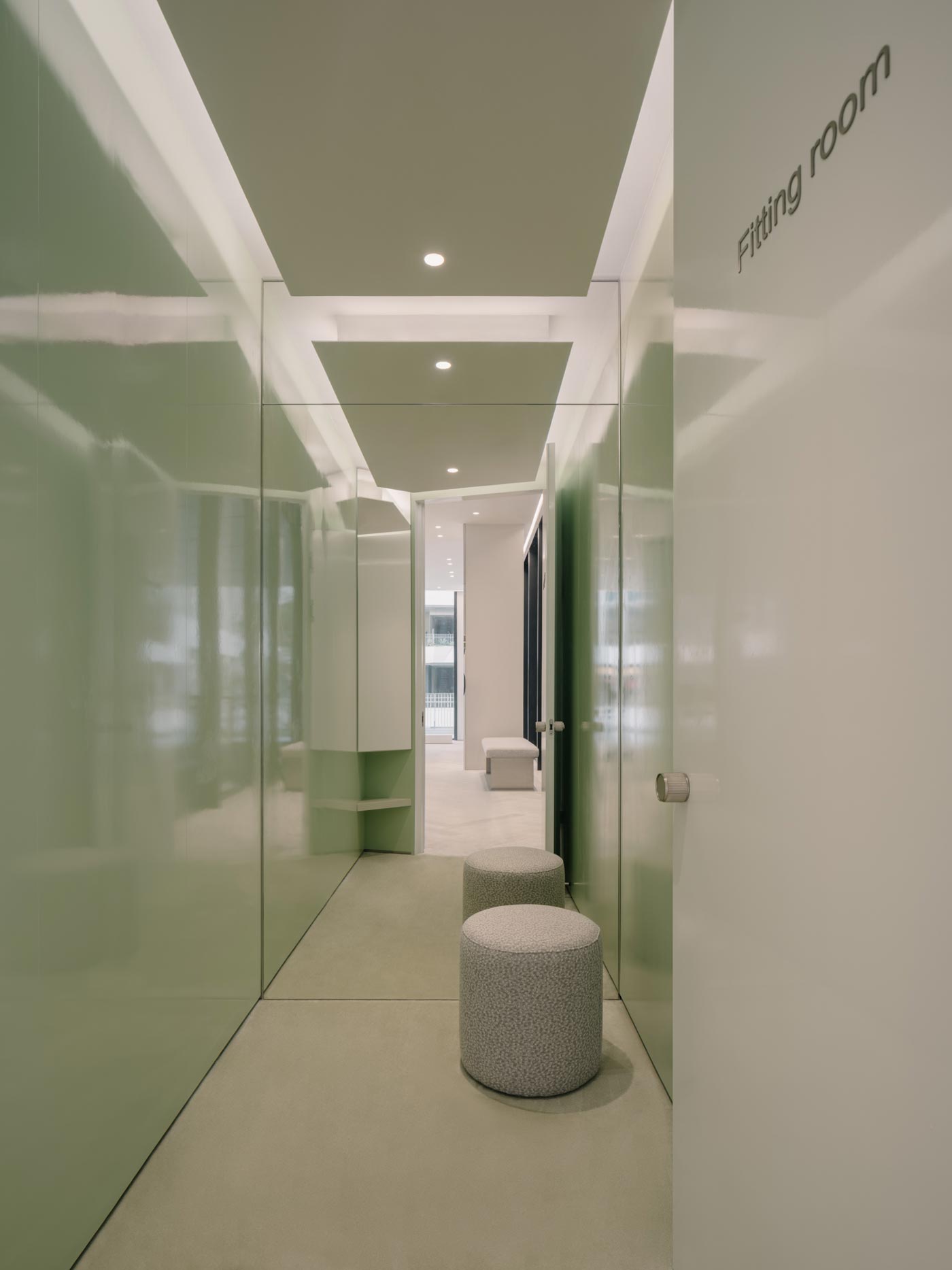 Fitting room corridor inside the sage flagship store in Shenzhen with glossy green surfaces, integrated lighting and cylindrical seating