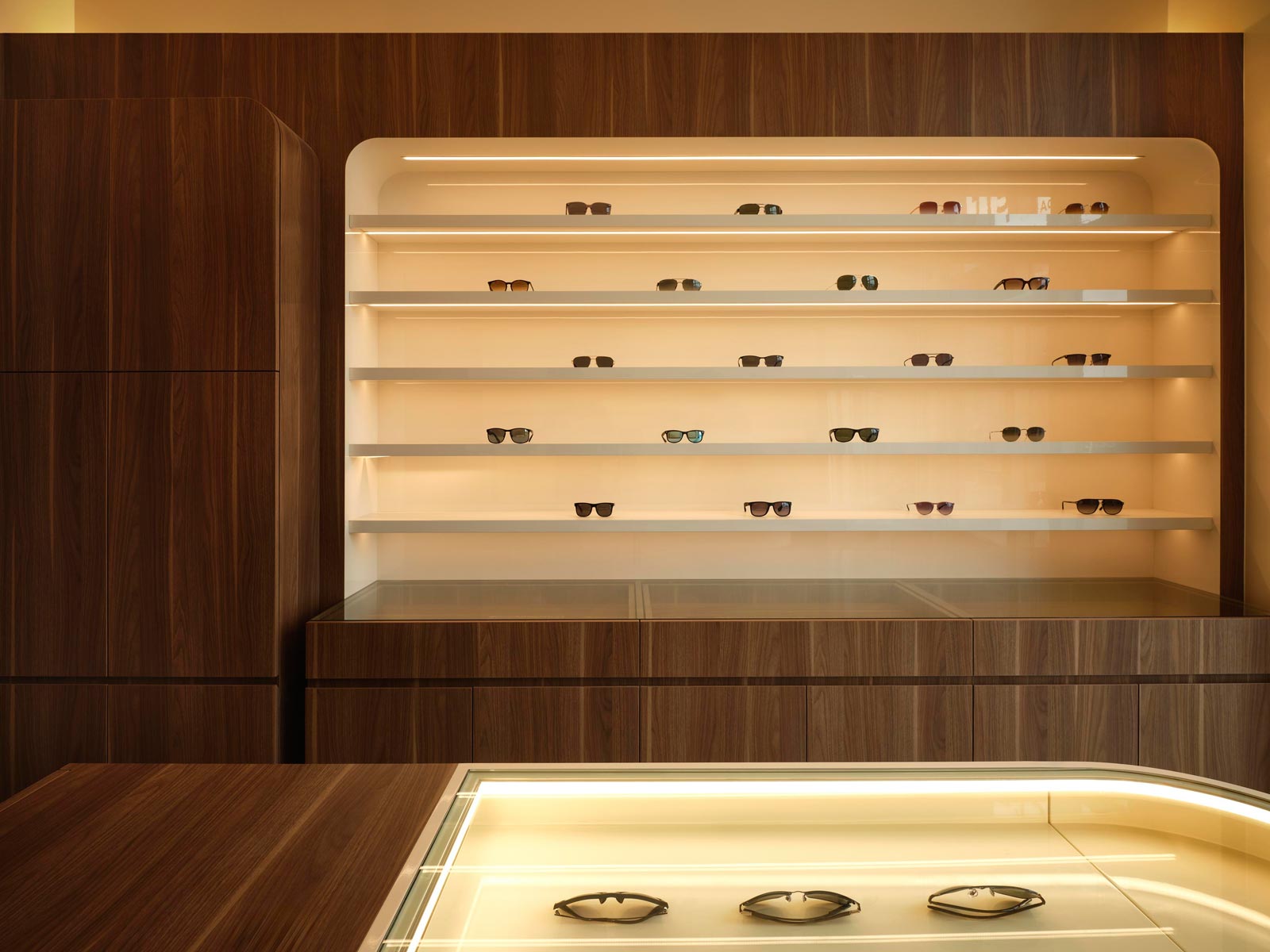 Sistemi espositivi stondati in legno di noce e finiture avorio nella boutique di ottica