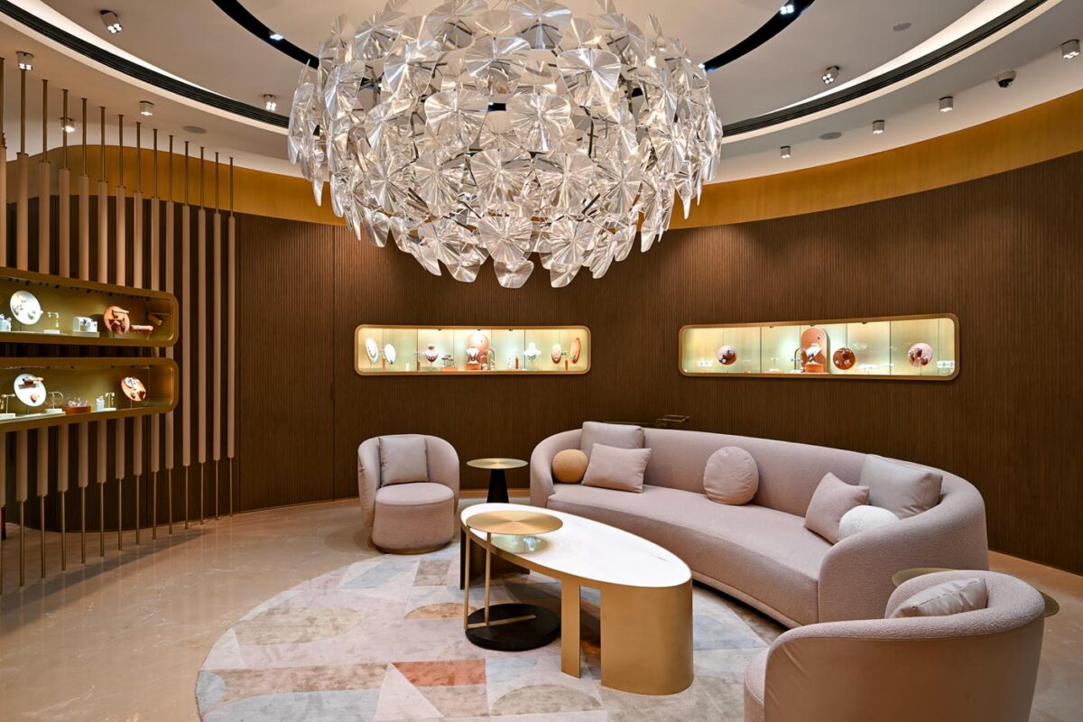 Contemporary jewellery store lounge with curved sofas, fluted wood walls, backlit display niches and sculptural chandelier, Eish Jewels Indore