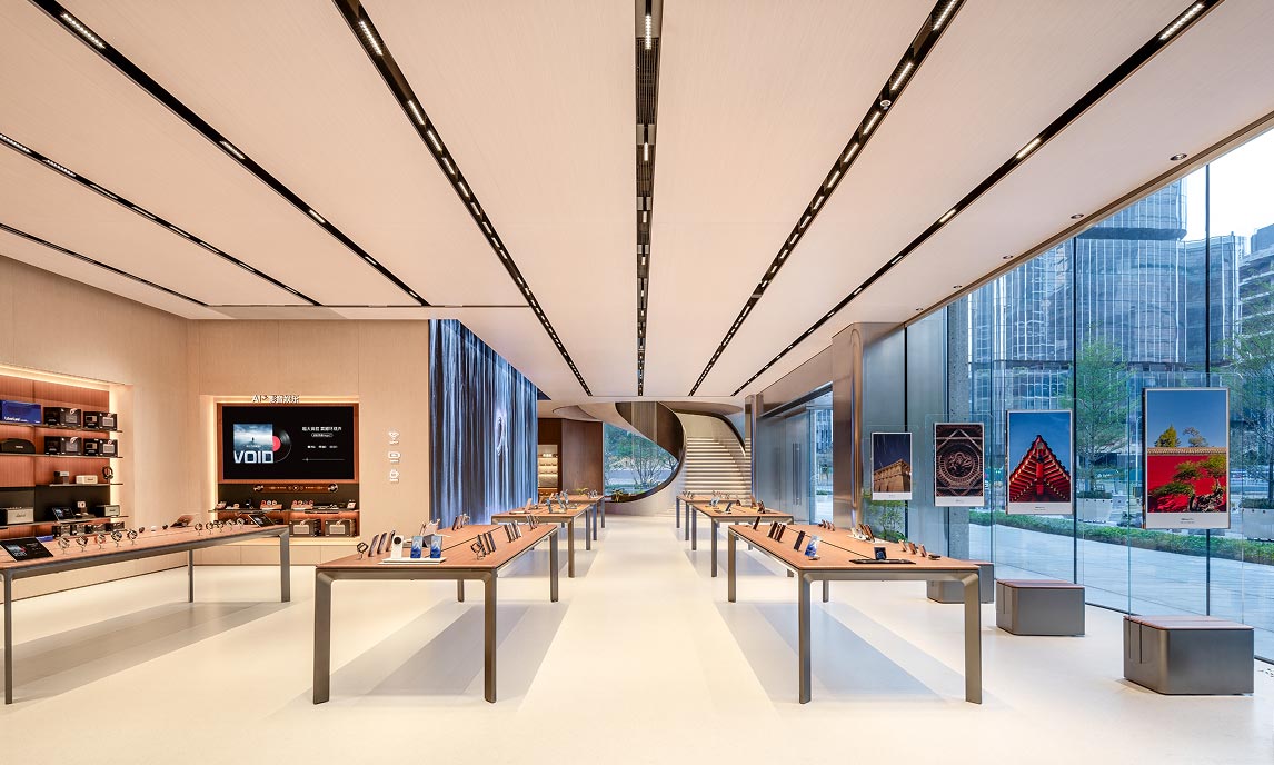 Vista longitudinale dell’interno dell’HONOR Flagship Store Shenzhen Bay con tavoli espositivi, vetrata continua e scala elicoidale sullo sfondo