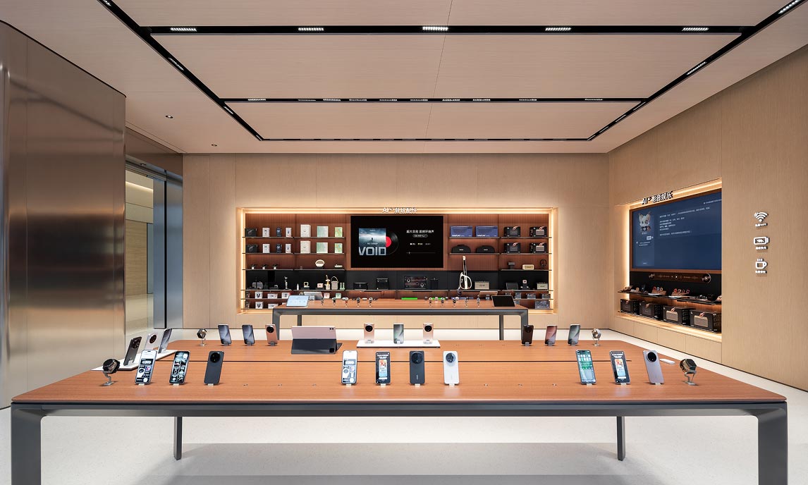 Area espositiva prodotti con tavolo centrale e pareti attrezzate illuminate all’interno dell’HONOR Flagship Store Shenzhen Bay