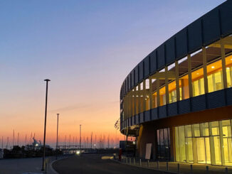 Vista esterna del Waterfront Mall di Genova al tramonto con facciata vetrata e affaccio sul porto