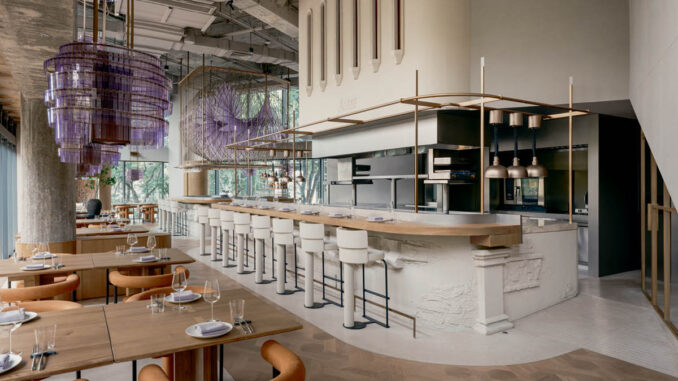 Ristorante Aster a Shanghai con bancone centrale circolare in argilla, cucina a vista e installazioni luminose sospese in tonalità viola