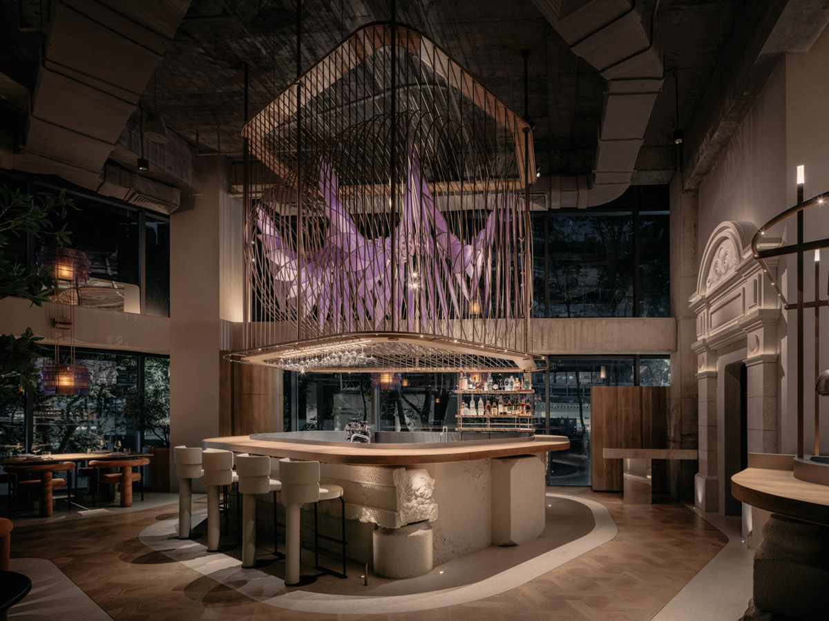 Central counter at Aster restaurant in Shanghai with suspended metal structure and purple petal-inspired lighting installation in a double-height space