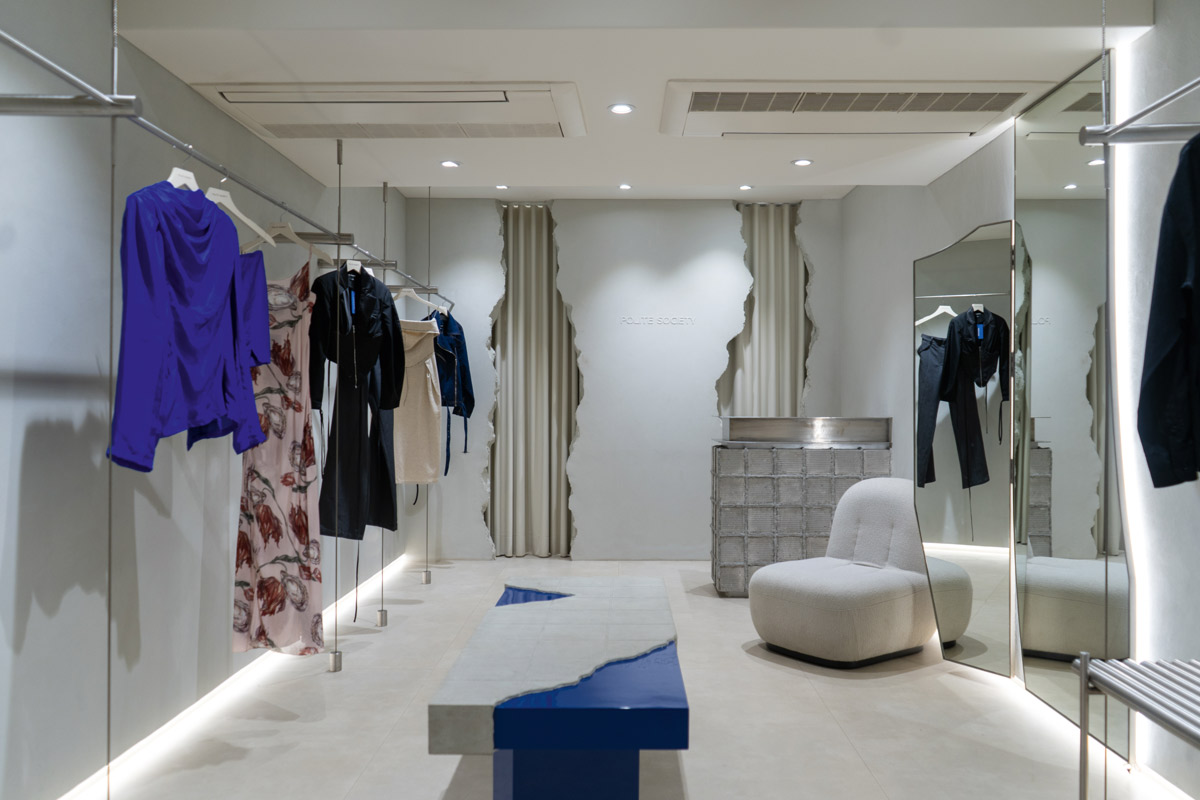 Fashion store interior with linear layout, suspended metal display systems, textured walls, mirrors and upholstered seating
