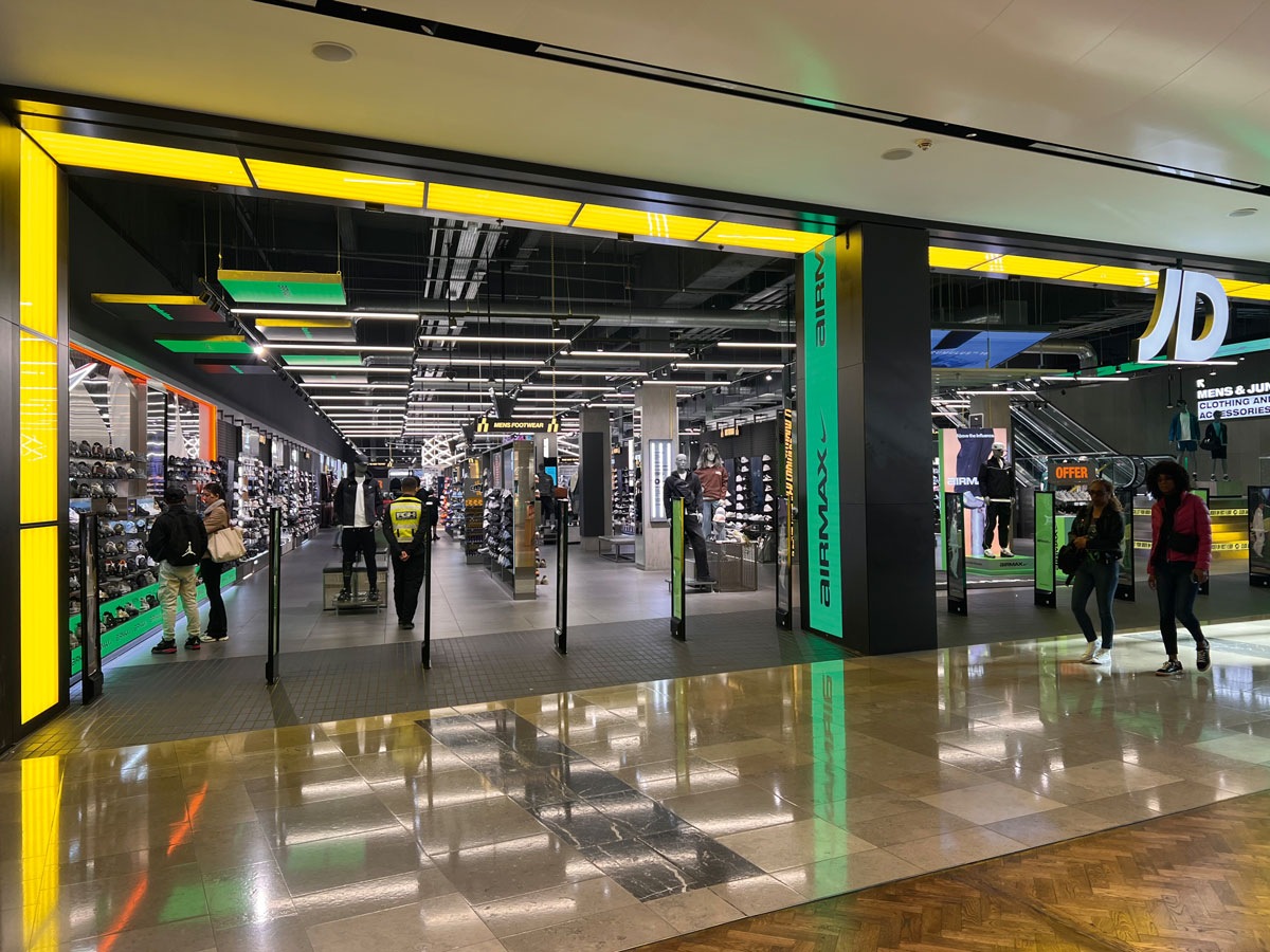 Ingresso JD Sports con lighting lineare e layout dedicato al footwear sportivo
