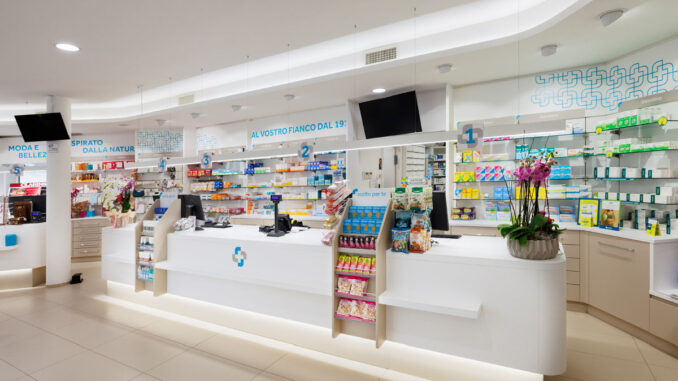 Area dermocosmesi in farmacia con espositori retroilluminati, banco consulenza e pavimento chiaro