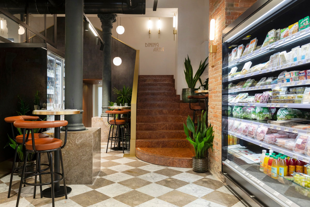Area consumazione del food retail a Palermo con sedute alte, pareti materiche e banco refrigerato