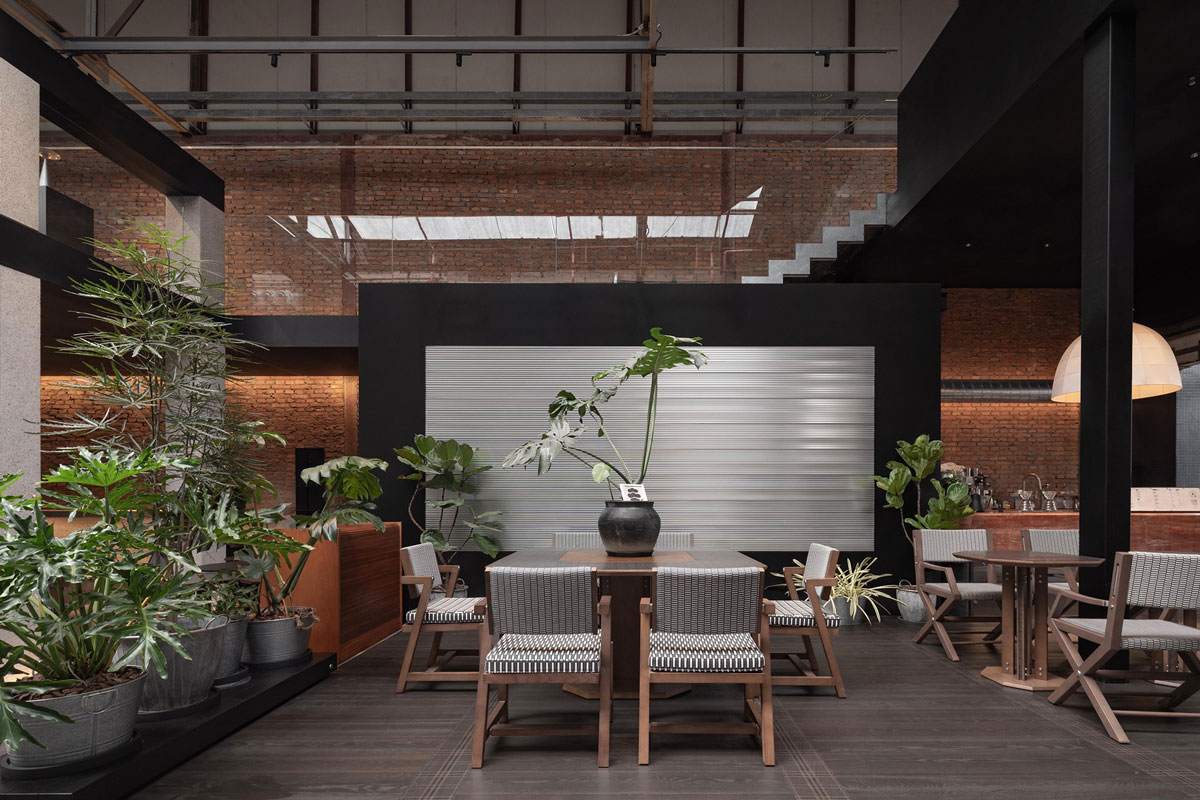 Lounge area inside TOMOSOON Cafe with communal table, tropical greenery, exposed brick walls and visible industrial structure