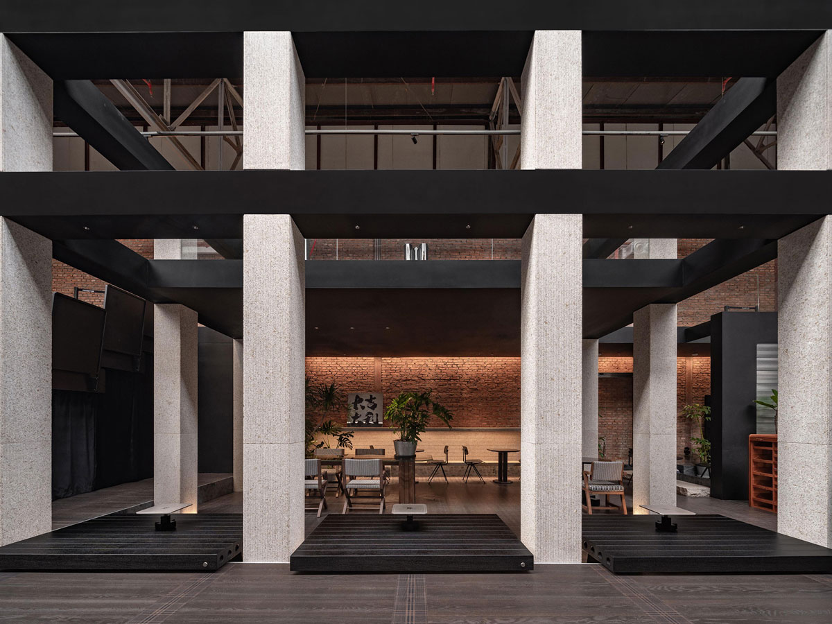 Interior architecture of TOMOSOON Cafe with clad columns, black wooden lounge platforms, exposed brick walls and double-height industrial structure