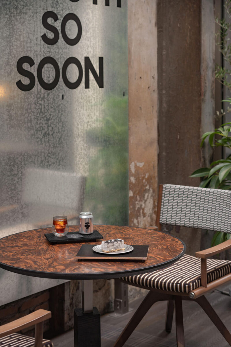 Bistro table inside TOMOSOON Cafe with wooden finishes, geometric textile seating and translucent metallic panels