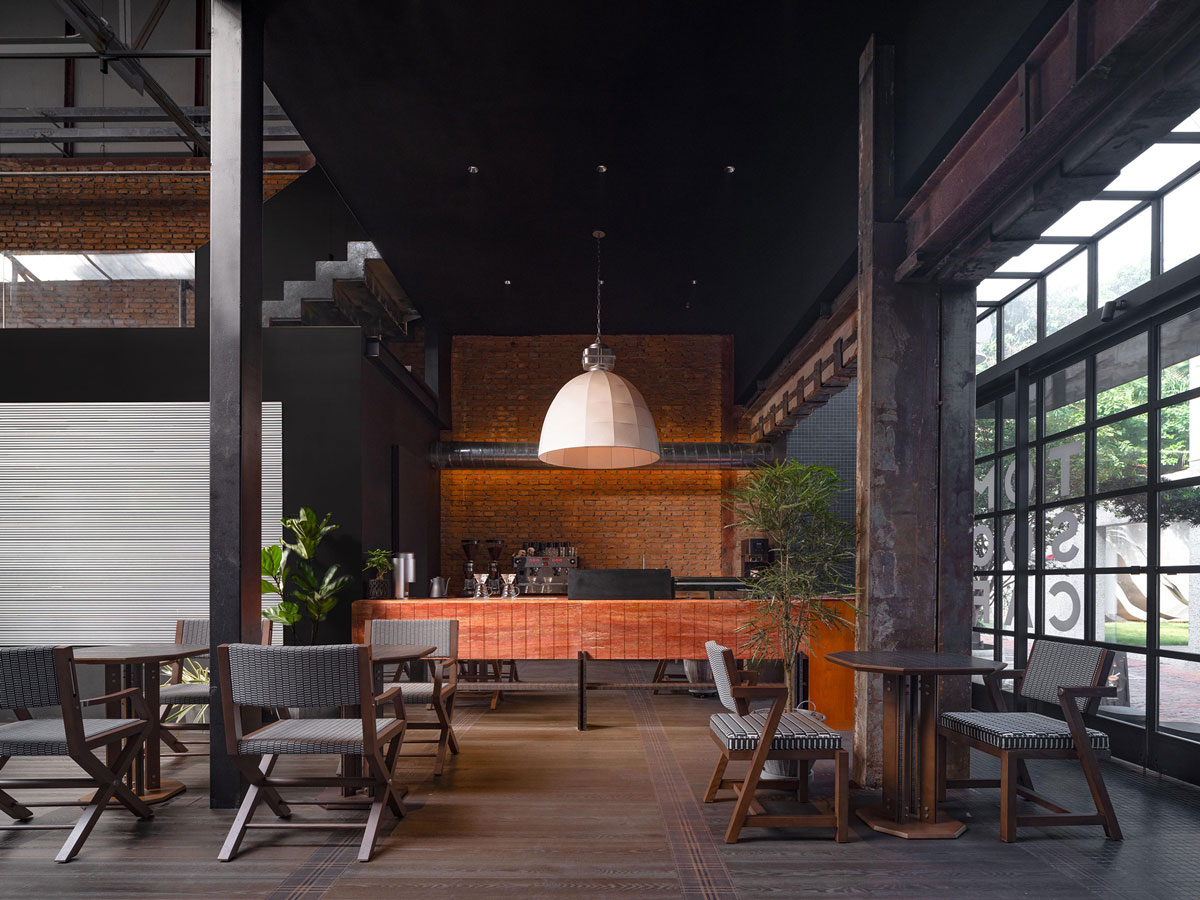 Seating area inside TOMOSOON Cafe with textured bar counter, exposed brick walls, suspended lighting and double-height industrial structure