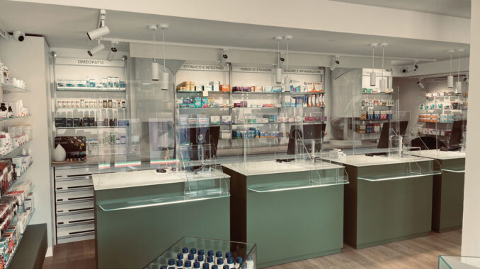 Vista laterale del banco farmacia con protezioni trasparenti e pareti espositive