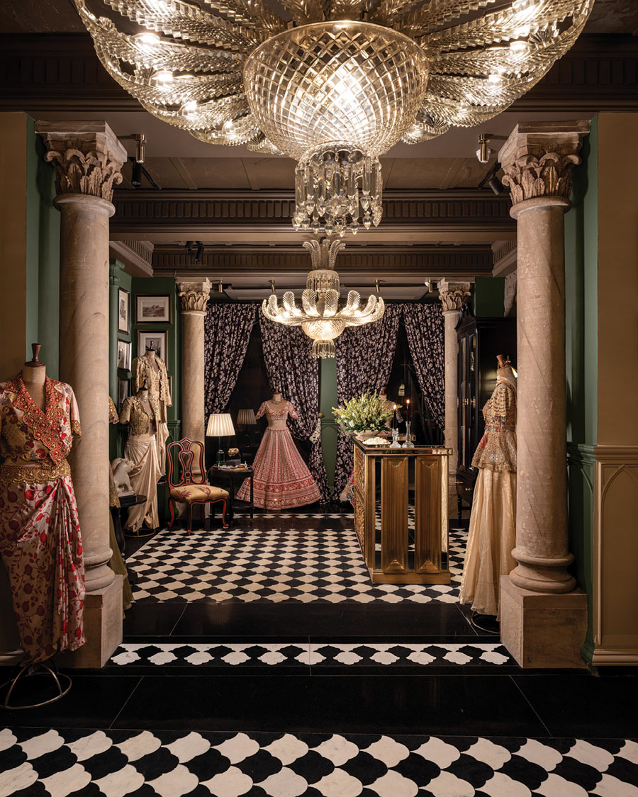 Gazal Gupta flagship area with column-framed niches, fabric curtains and couture garments lit by a decorative chandelier.