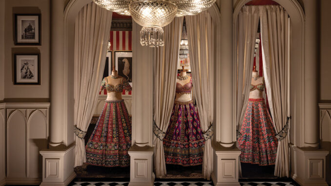 Area espositiva del flagship GG Fort di Gazal Gupta con nicchie scandite da colonne, tende in tessuto e abiti couture illuminati da lampadario decorativo.