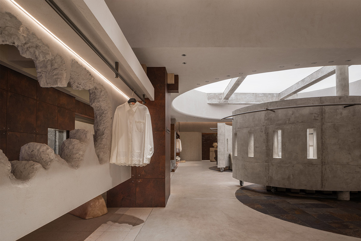Sculpted display wall in the Hé showroom with a suspended garment, curved concrete structure and overhead skylight
