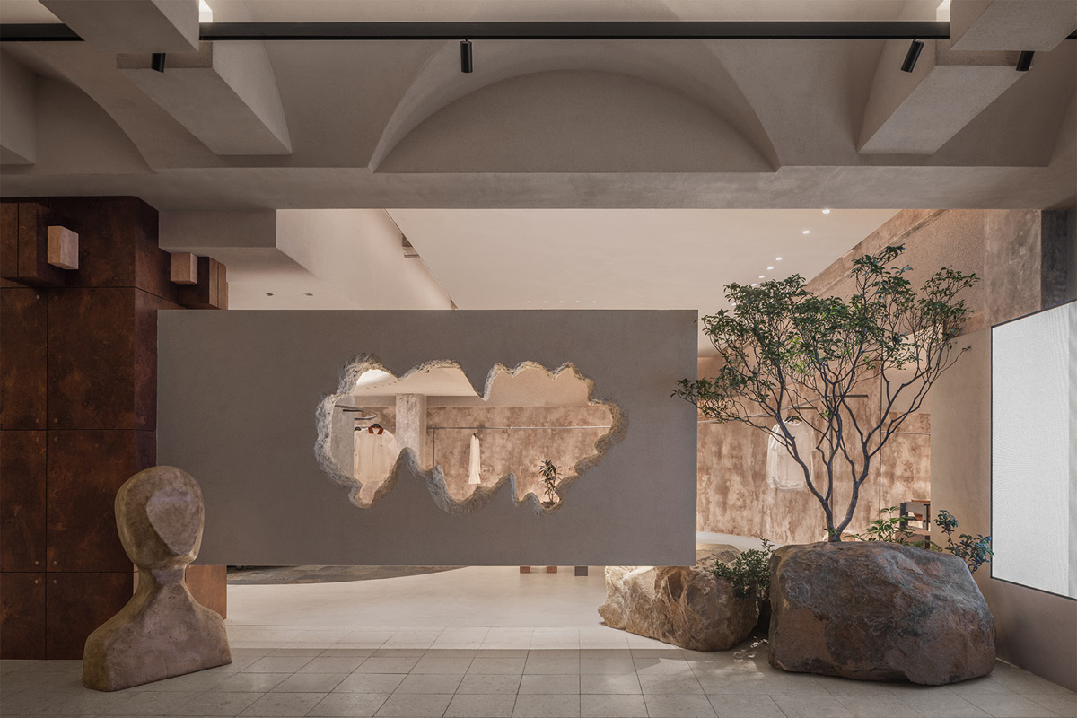 Suspended volume with a sculptural opening in the Hé showroom, flanked by a tree and large natural stones