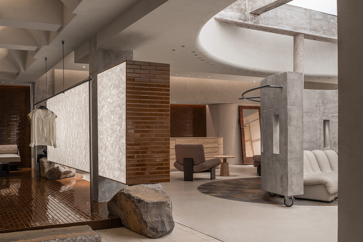 Circulation area in the Hé showroom with backlit surfaces, curved concrete structures, skylight and natural stone
