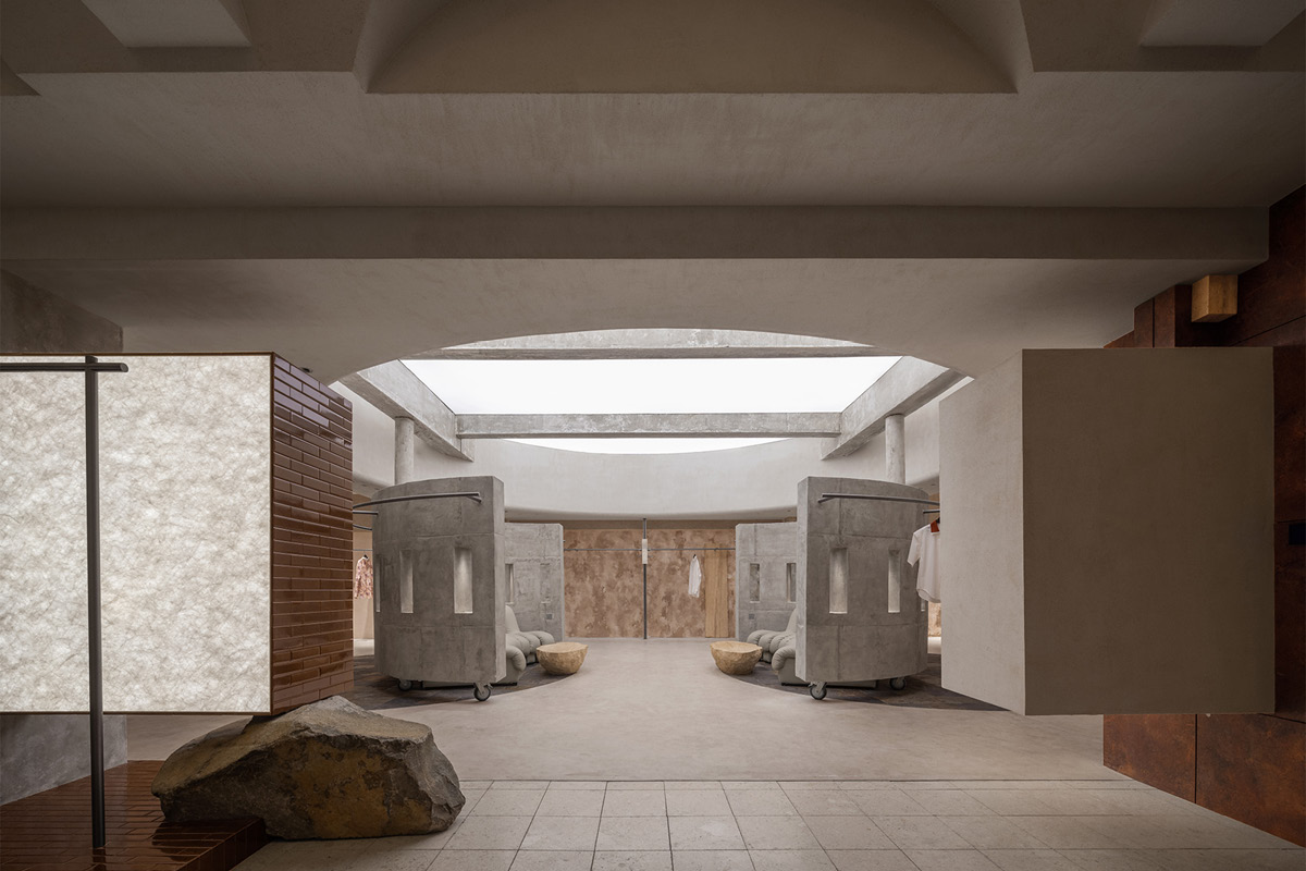 Axial view of the Hé showroom with an overhead skylight, curved concrete volumes and central circulation axis