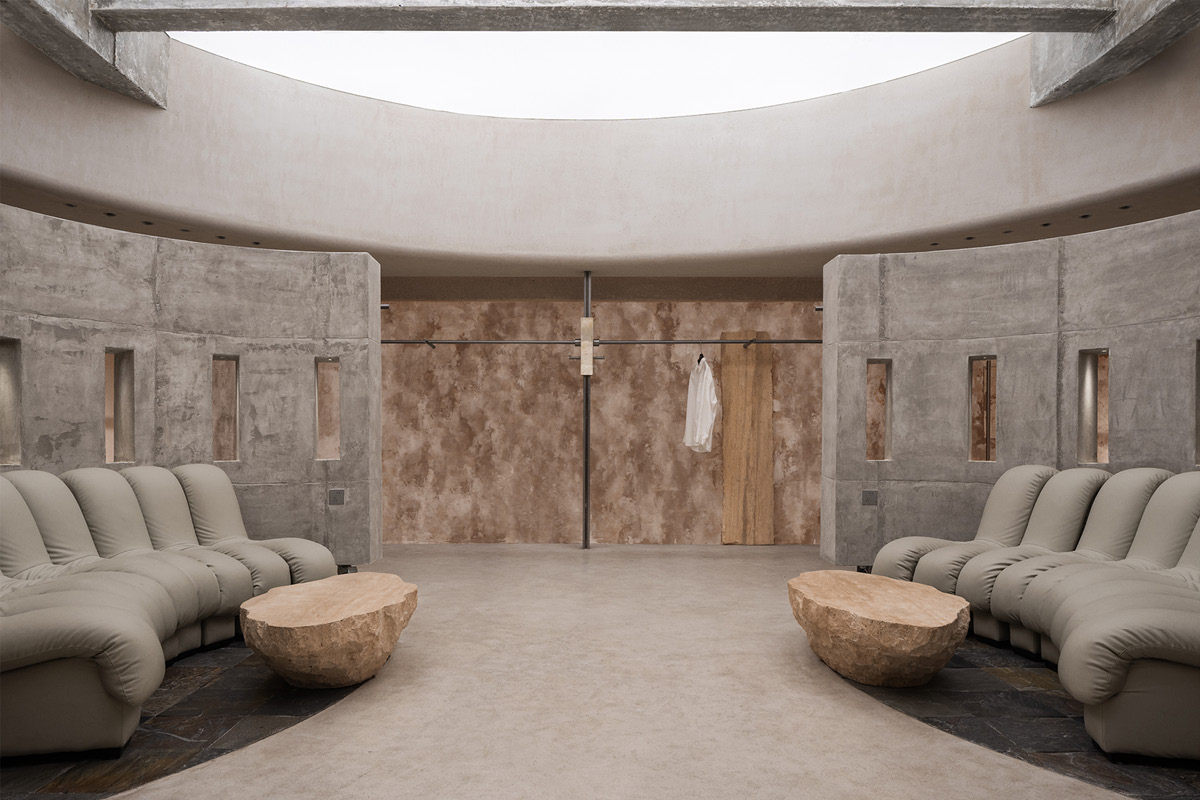 Lounge area in the Hé showroom with facing seating, curved concrete structures and an overhead skylight