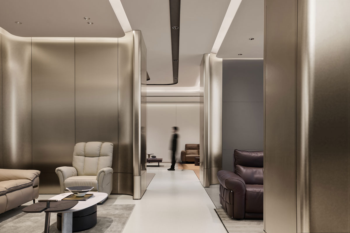 Interior circulation in the KUKA | JOY Living & Dining Showroom with satin-finished metal surfaces, integrated lighting and living settings arranged along the exhibition layout.