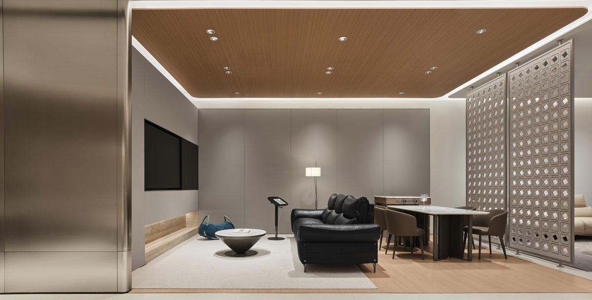 Living and dining area of the KUKA | JOY Living & Dining Showroom with a leather sofa, dining table, wood ceiling, perforated partition and integrated lighting.