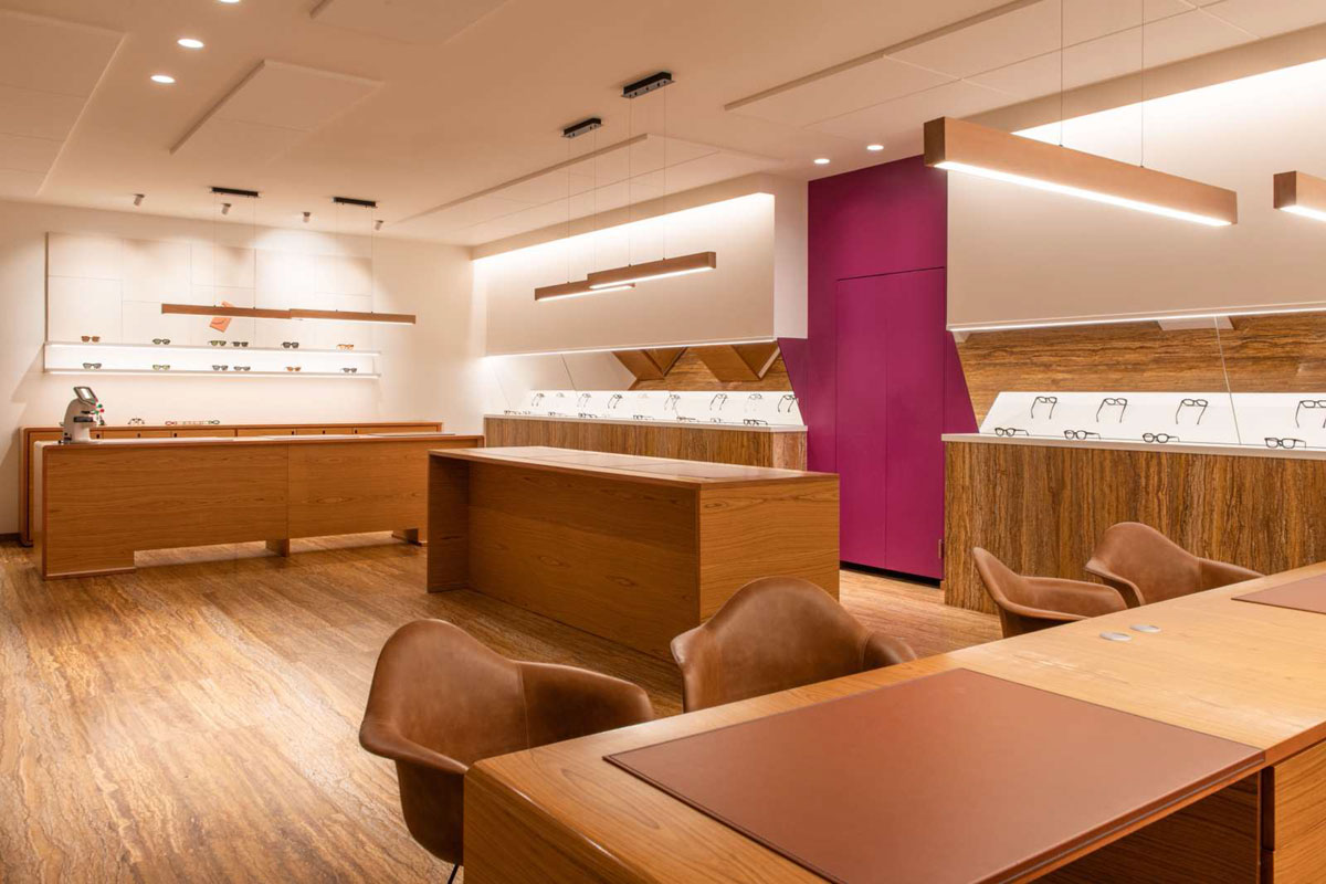 Area espositiva di Ottica Adami con arredi in legno recuperati, isola centrale, tavolo per la consulenza e illuminazione integrata.