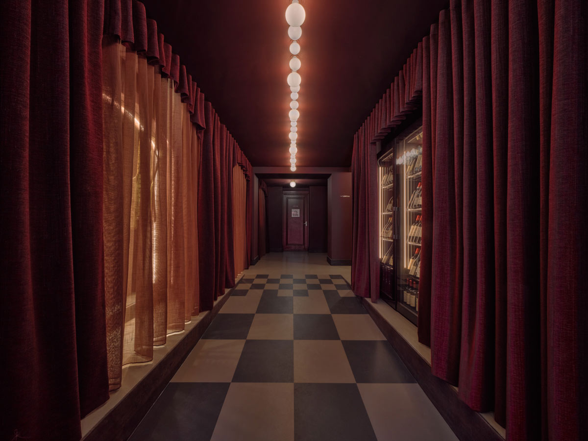 Corridoio di Café Vertigo con tende bordeaux e illuminazione lineare