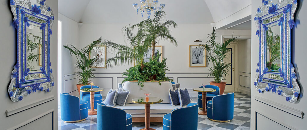 Hall dell’Hotel du Tasso a Sorrento progettata da Antonio Girardi, con sedute blu, specchi veneziani e vegetazione centrale.