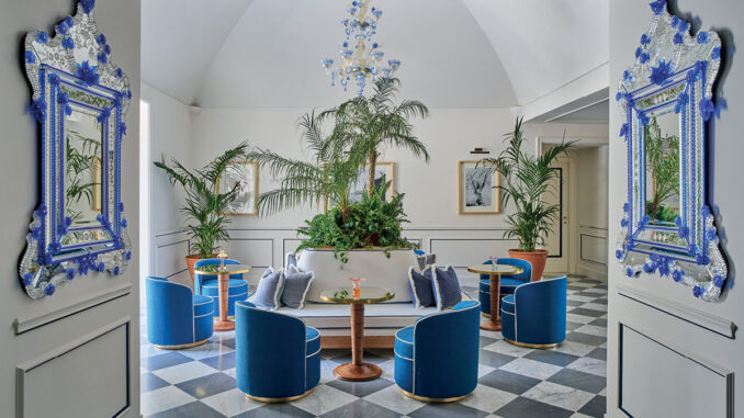Hall dell’Hotel du Tasso a Sorrento progettata da Antonio Girardi, con sedute blu, specchi veneziani e vegetazione centrale.