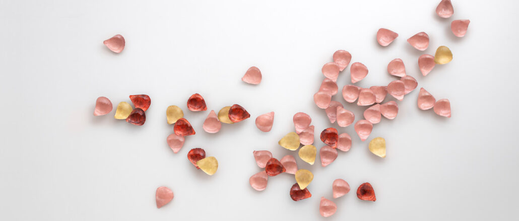 Floem di De Castelli, rivestimento decorativo tridimensionale composto da petali metallici rosa, rossi e dorati su parete bianca.