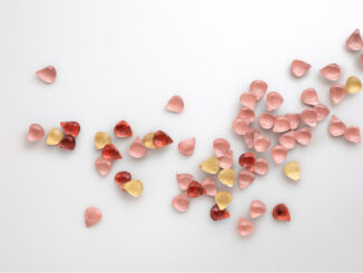 Floem di De Castelli, rivestimento decorativo tridimensionale composto da petali metallici rosa, rossi e dorati su parete bianca.