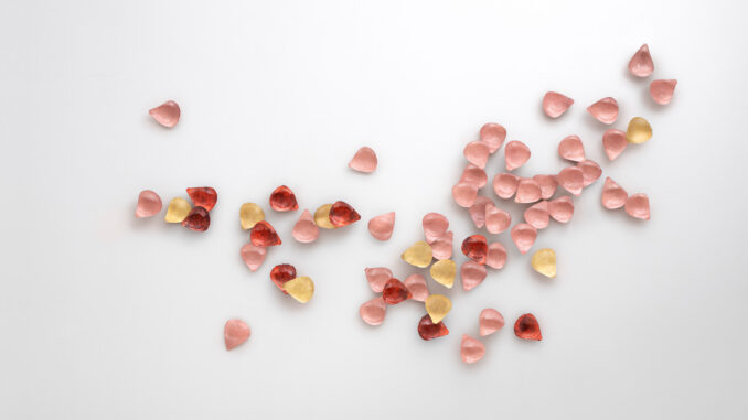 Floem di De Castelli, rivestimento decorativo tridimensionale composto da petali metallici rosa, rossi e dorati su parete bianca.